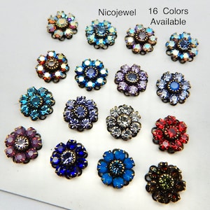 May include: A collection of sixteen flower-shaped rhinestone embellishments in various colors. Each jewel has a central stone surrounded by petals of smaller rhinestones. The text "Nicojewel" and "16 Colors Available" are visible.