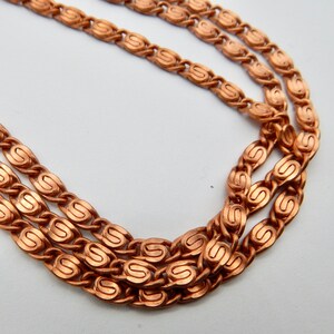 May include: A copper chain necklace with a detailed, ornate design. The chain is made of multiple strands of linked oval shapes.