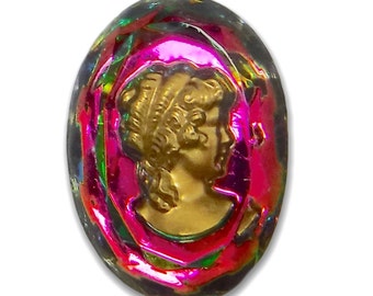 Könnte beinhalten: Ovaler, irisierender Glas-Cameo mit rosa und grünem Hintergrund. Der Cameo zeigt ein goldenes Profil einer Frau mit nach hinten gekämmten Haaren.
