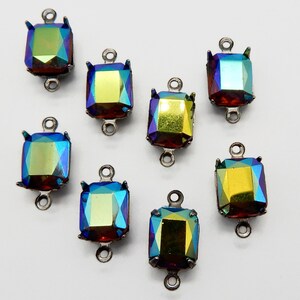 May include: Eight iridescent, faceted, square-shaped glass charms with silver-toned metal loops. The charms have a rainbow effect with shades of blue, green, and gold.