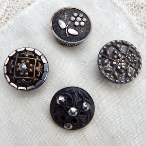 May include: Four antique buttons with intricate designs. One button features a floral pattern with silver accents, while another has a square design with a central gem. The other two buttons have detailed patterns and silver accents.