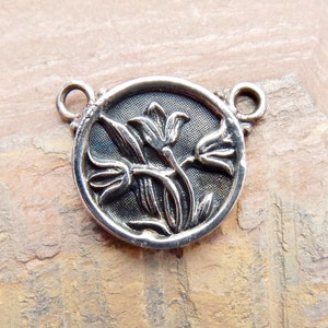 May include: Silver-toned metal charm featuring a detailed design of three stylized tulips. The charm has two loops for attaching to a necklace or bracelet.