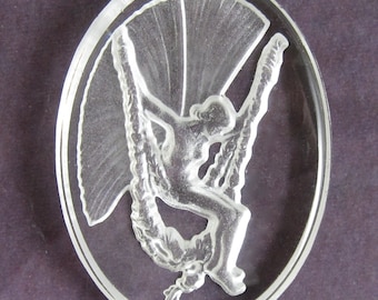May include: A clear glass oval pendant with a raised design of a woman sitting on a swing with a fan-shaped design behind her.