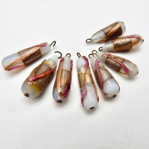 May include: Eight white glass beads with gold and pink accents and brass loops. The beads are teardrop shaped and have a mottled appearance.