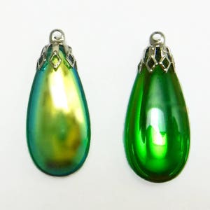 May include: Two teardrop-shaped glass pendants with silver metal caps. The pendant on the left is iridescent green and gold, while the pendant on the right is solid green.