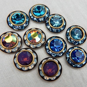 May include: A collection of ten decorative buttons with jewel-toned center stones. The buttons feature a gold-colored rim and a dark outer ring. The center stones are various shades of blue, purple, and iridescent colors.