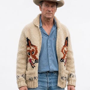Può includere: Un cardigan in maglia beige con zip e grafica di volpe su entrambi i lati, indossato sopra una camicia azzurra e jeans blu, abbinato a un cappello da cowboy beige. Il cardigan presenta un collo a scialle, polsini a coste e due tasche.