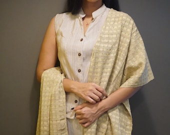 May include: A woman wearing a beige sleeveless blouse with a button-up collar and a beige and white checkered shawl. The shawl has a fringe border.