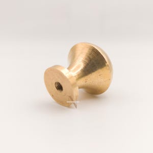 Pode incluir: Um puxador de armário de latão maciço com um design arredondado em forma de cogumelo. O puxador tem uma base roscada para fácil instalação. O acabamento em latão confere-lhe um aspeto clássico e intemporal, adequado para vários estilos de mobiliário.