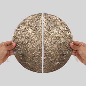 May include: Two bronze-coloured, semi-circular door handles with a textured, crumpled appearance. The handles are held up against a light grey background, showcasing their unique design and metallic finish. The handles are likely for a cabinet or door.