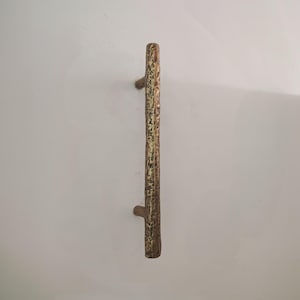 May include: A rustic, vertical door pull handle with a textured, bark-like appearance. The handle is primarily gold with brown accents, and has a branch-like design. The handle is approximately 12 inches long.