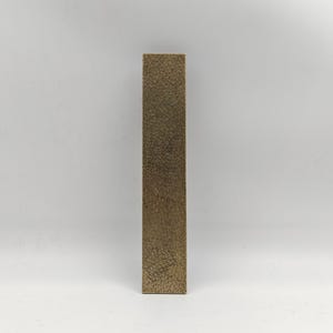 May include: A tall, rectangular object with a textured, golden-brown surface. The object stands upright against a plain white background. The texture appears to be made up of many small, closely packed elements.