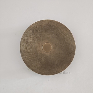 Może przedstawiać: Okrągła dekoracja ścienna w kolorze brązu. Teksturowana powierzchnia ma wzór koncentrycznych okręgów, z mniejszym, okrągłym detalem pośrodku. Ten nowoczesny element pasuje do różnych stylów wnętrz.