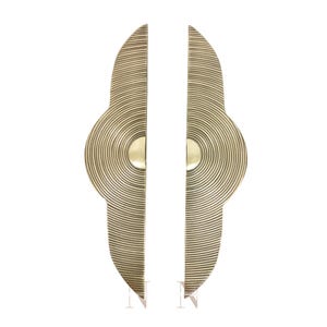May include: Two brass-colored door handles with a unique design. Each handle is shaped like a half-oval with concentric circular grooves. A circular accent is centered on each handle, creating a modern, artistic look. The handles are designed for a door.