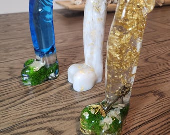 May include: Three decorative resin sculptures in the shape of a phallus. One is blue with green and white accents, another is white with gold leaf, and the third is clear with gold leaf and a small key.
