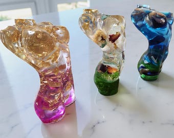 May include: Three resin sculptures in the shape of a torso. One is gold and pink with gold leaf, the second is clear with dried flowers and green base, and the third is blue with green base.