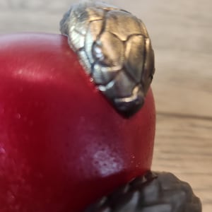 May include: A close-up of a red object with a silver-colored snake head design. The snake head is detailed with textured scales. The object appears to be a decorative item or part of a larger piece.