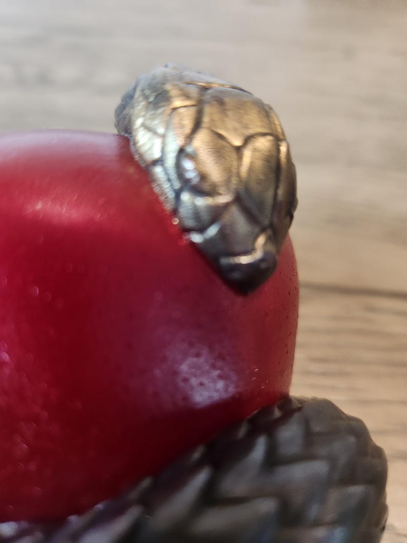 May include: A close-up of a red object with a silver-colored snake head design. The snake head is detailed with textured scales. The object appears to be a decorative item or part of a larger piece.