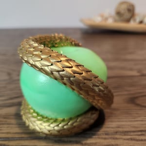 May include: A gold-colored, textured snake wraps around a light green sphere. The snake's scales are detailed, and the sphere has a smooth surface. The design is set against a blurred background.