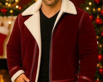 May include: A burgundy jacket with a cream-colored shearling collar and trim. The jacket has a zipper closure and is worn over a black V-neck shirt. The model is wearing blue jeans. The background includes a Christmas tree and festive decorations.
