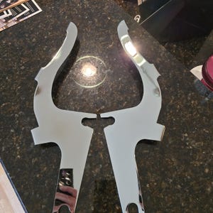 Könnte beinhalten: Zwei verchromte Motorrad-Sissy-Bar-Halterungen. Die Halterungen sind U-förmig und haben eine glatte, glänzende Oberfläche.