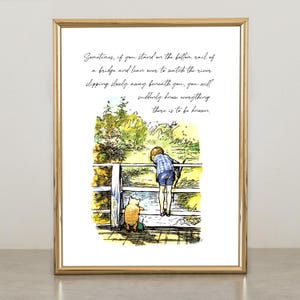 May include: A framed print with a gold border featuring a watercolor illustration. The artwork depicts a young person and a bear looking over a fence at a river. The print includes handwritten text.