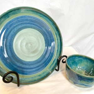 May include: A set of handmade ceramic dishes in shades of blue and green. The larger dish has a swirling pattern and the smaller bowl has a more mottled glaze.