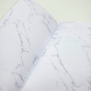 May include: An open notebook with a white marble pattern on the cover and pages.