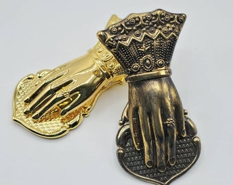 May include: Two gold-toned metal hand-shaped paperweights. One is gold and the other is a darker gold with a crown on the back of the hand.