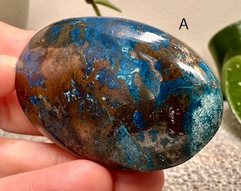May include: A polished, oval-shaped stone with a mix of blue, brown, and silver colors. The stone has a glossy finish and a natural, textured appearance. The letter "A" is visible on the stone. This item is a decorative stone.