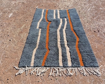 Könnte beinhalten: Ein rechteckiger, dunkelblauer Teppich mit strukturierter Oberfläche. Der Teppich hat vertikale Streifen in Beige und Orange, mit Fransen am unteren Rand. Der Teppich liegt auf einer braunen Oberfläche.