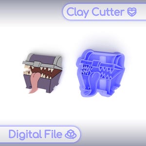 Pode incluir: Um baú de tesouro de desenho animado roxo e cinza com dentes afiados e uma língua rosa, ao lado de um cortador de argila azul em forma de baú. Os textos "Clay Cutter" e "Digital File" são visíveis.