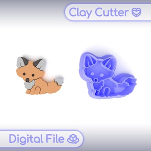 Może przedstawiać: Wycinak do gliny i gotowa figurka lisa z gliny. Figurka lisa jest pomarańczowa z szarymi i białymi akcentami. Wycinak jest niebieski i w kształcie lisa. Tekst "Clay Cutter" i "Digital File" znajdują się na zdjęciu.