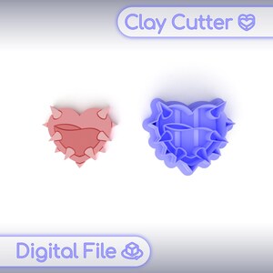 Puede incluir: Dos cortadores de arcilla en forma de corazón. Uno es rosa con púas, el otro es azul con un diseño similar. El texto "Clay Cutter" y "Digital File" es visible.