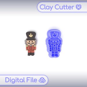 May include: A clay cutter and a finished clay figure of a nutcracker soldier. The cutter is blue, and the finished figure is red, black, and tan. The text "Clay Cutter" and "Digital File" are visible.
