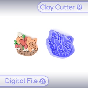 以下が含まれることがあります： バスケットに入ったキツネのデザインのクレイカッターと完成したクレイ作品。完成品はオレンジ、赤、緑の色合いです。カッターは青色で、「Clay Cutter」と「Digital File」の文字が入っています。