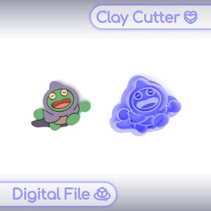 Peut inclure: Deux emporte-pièces en argile, l'un est un produit fini et l'autre un moule, tous deux en forme de personnage de dessin animé avec une cape à capuche. Le produit fini est vert, violet et marron. Le moule est bleu. Le texte "Clay Cutter" et "Digital File" sont visibles.
