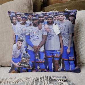May include: A decorative pillow featuring a group of basketball players in gray t-shirts and blue shorts. The shirts read "Finals" and "Oklahoma City Thunder". The players are holding a trophy.
