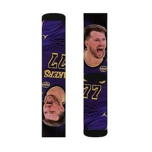 May include: A pair of purple and gold basketball socks. One sock features a player's face and the number 77 in gold. The other sock has the number 77 and the word "Lakers" in gold. The socks have a black cuff.