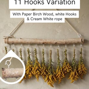 May include: A wall-hanging display featuring a natural paper birch wood branch suspended by a cream white rope. Eleven white metal hooks are attached to the branch, each holding a bundle of dried yellow flowers. Text reads 11 Hooks Variation.