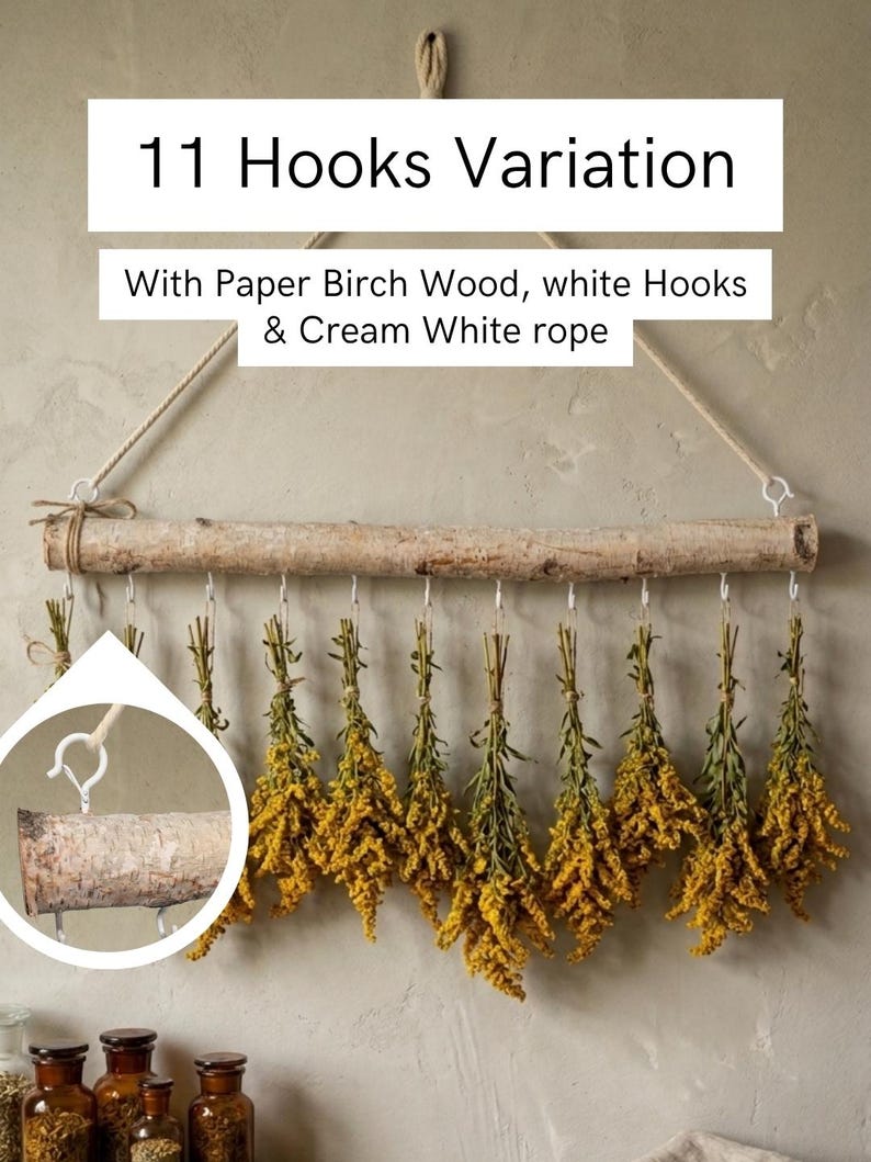 May include: A wall-hanging display featuring a natural paper birch wood branch suspended by a cream white rope. Eleven white metal hooks are attached to the branch, each holding a bundle of dried yellow flowers. Text reads 11 Hooks Variation.