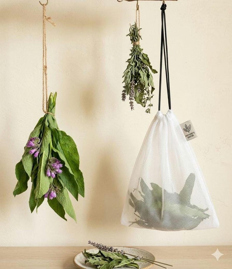May include: A white mesh drawstring bag containing green leaves, hanging next to a bundle of green leaves with purple flowers and a bundle of dried herbs. A small tag on the bag features a leaf icon and the text "WETSIE'S DOTON".