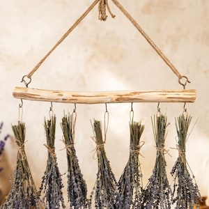 May include: A wall hanging display featuring a light-colored wooden branch suspended by a jute rope. Seven bundles of dried purple lavender are tied with twine and hung from the branch using small metal hooks attached to the wood.