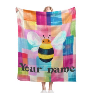 May include: A colourful fleece blanket with a yellow and black bee illustration and the text "Your name".