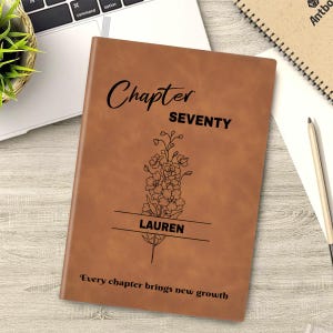 May include: A brown leather journal with the words "Chapter Seventy" and "Lauren" engraved on the cover. A floral design is etched below the text. The phrase "Every chapter brings new growth" is printed at the bottom.