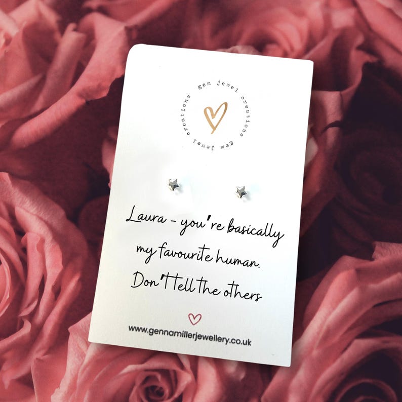 Pode incluir: Um cart&atilde;o branco com brincos em forma de estrela e o texto "Laura - voc&ecirc; &eacute; basicamente minha pessoa favorita. N&atilde;o conte aos outros". O cart&atilde;o est&aacute; sobre um fundo de rosas cor-de-rosa.