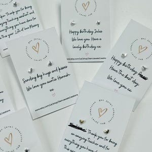 Pode incluir: V&aacute;rios cart&otilde;es de felicita&ccedil;&otilde;es com brincos pequenos. Os cart&otilde;es t&ecirc;m um logotipo de cora&ccedil;&atilde;o e textos como "Feliz anivers&aacute;rio" e "Obrigado". Os brincos s&atilde;o prateados e dourados em v&aacute;rias formas.