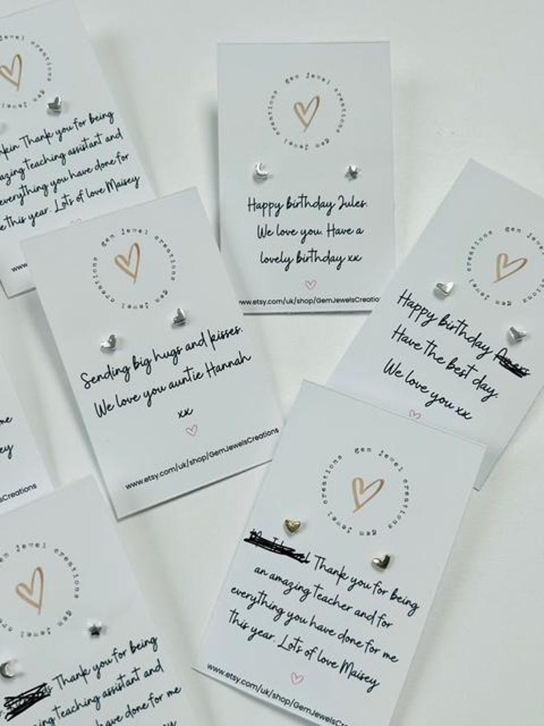 Pode incluir: V&aacute;rios cart&otilde;es de felicita&ccedil;&otilde;es com brincos pequenos. Os cart&otilde;es t&ecirc;m um logotipo de cora&ccedil;&atilde;o e textos como "Feliz anivers&aacute;rio" e "Obrigado". Os brincos s&atilde;o prateados e dourados em v&aacute;rias formas.