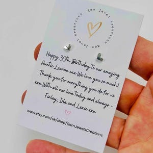 Pode incluir: Brincos pequenos em forma de cora&ccedil;&atilde;o prateado em um cart&atilde;o branco. O cart&atilde;o tem texto manuscrito desejando um feliz 30&ordm; anivers&aacute;rio. O cart&atilde;o tamb&eacute;m tem um logotipo de cora&ccedil;&atilde;o dourado e o URL da loja Etsy.