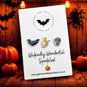 May include: A white display card featuring three stud earrings: a black bat, a gold cat, and a silver skull. The card displays the text "gem jewel creations", "Wickedly Wonderful Sparkles!", a pumpkin icon, and "www.gennamillerjewellery.co.uk".